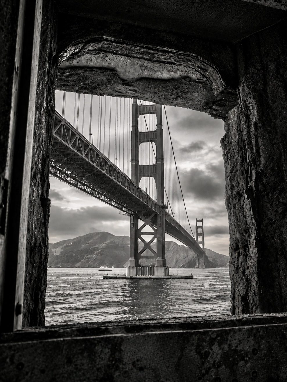 The Golden Gate Bridge framed through a window opening in a stone wall, in black and white
